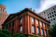 A Victorian red brick building in a bustling urban cityscape with a blue sky backdrop.
